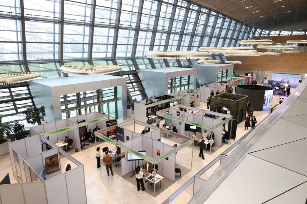 An aerial view of a large exhibition hall with rows of display booths and visitors walking between them
