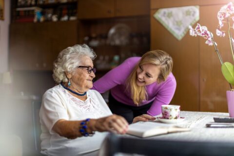 Young woman leaning in and laughing with an older woman at a table with a cup of tea and an open book