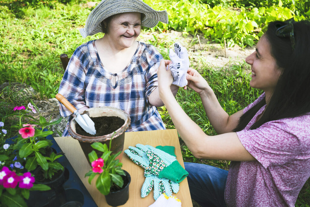 Support worker and a smiling woman with a disability potting flowers together in the garden