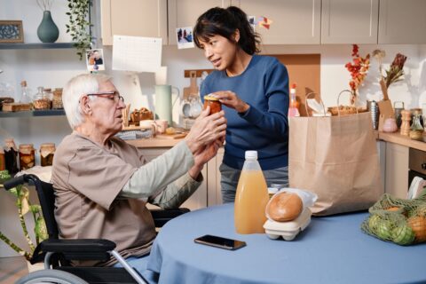 Support worker helping an older man in a wheelchair unpack groceries in his kitchen