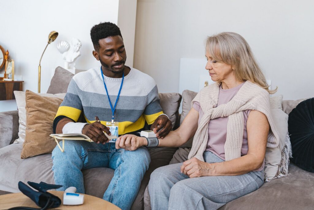 Carer with a lanyard sitting beside an older woman on a sofa during a home visit