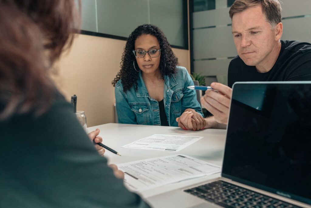 A couple listening as a person explains documents on a table with a laptop open