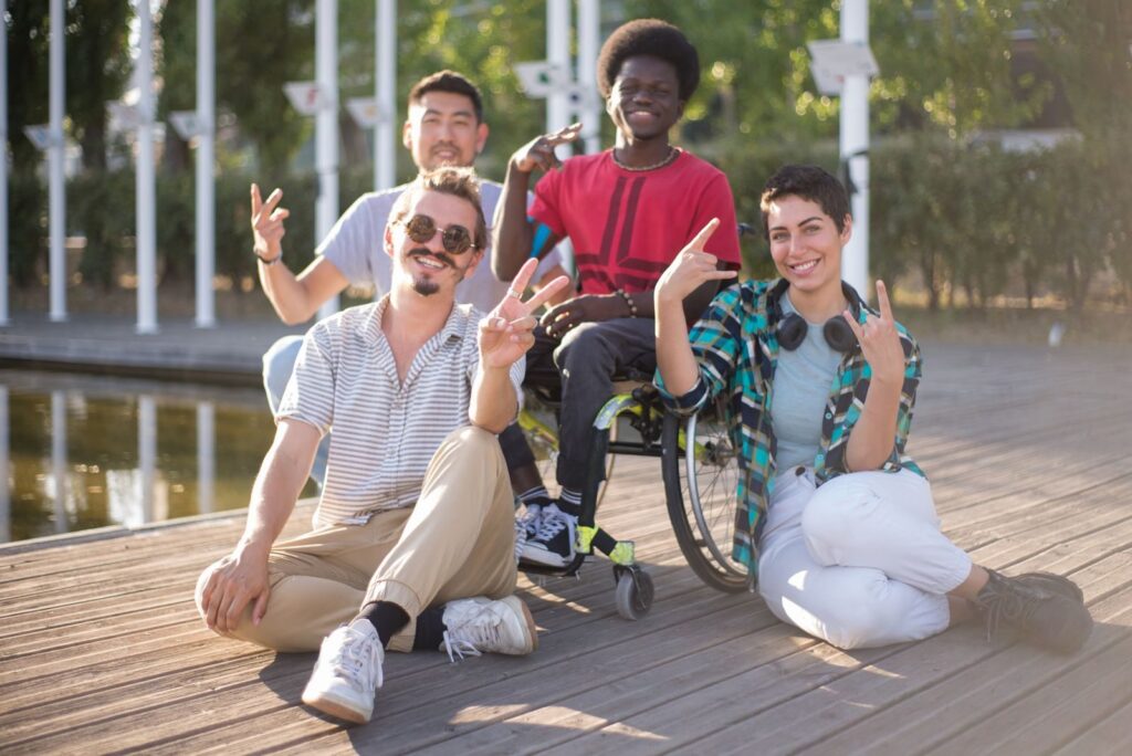 A group of smiling friends sitting together on an outdoor deck, one of them in a wheelchair