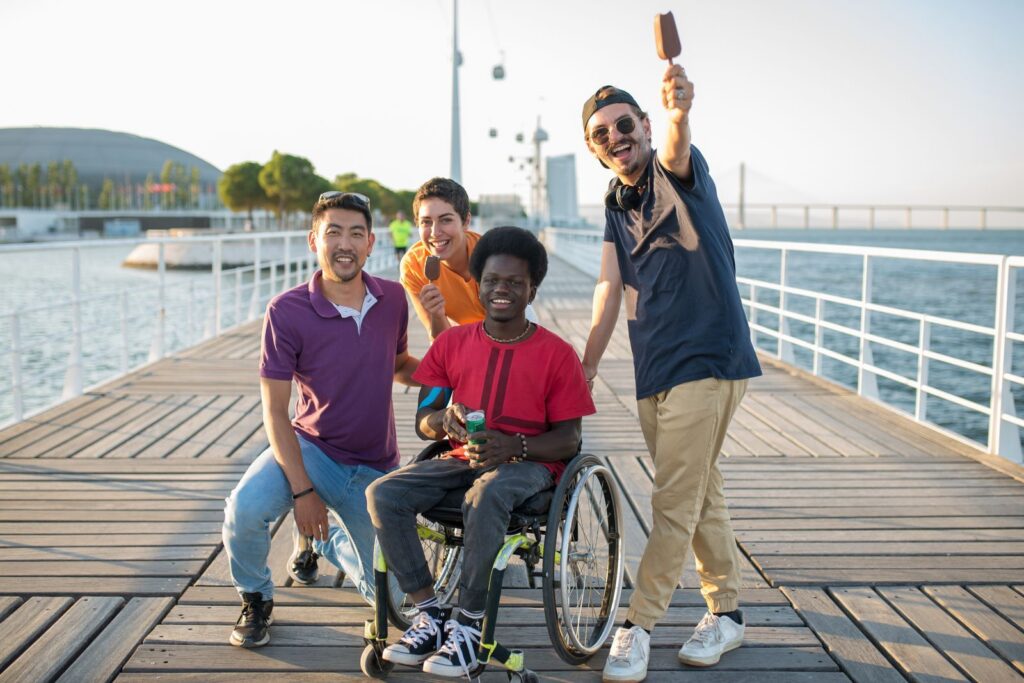 Friends laughing together on a waterfront pier, one of them in a wheelchair