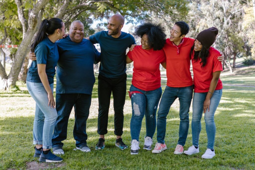 A group of people standing arm in arm and smiling together on a park lawn