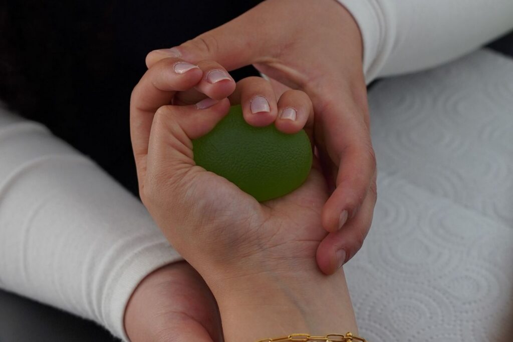Two hands holding a small green therapy ball during a hand exercise session