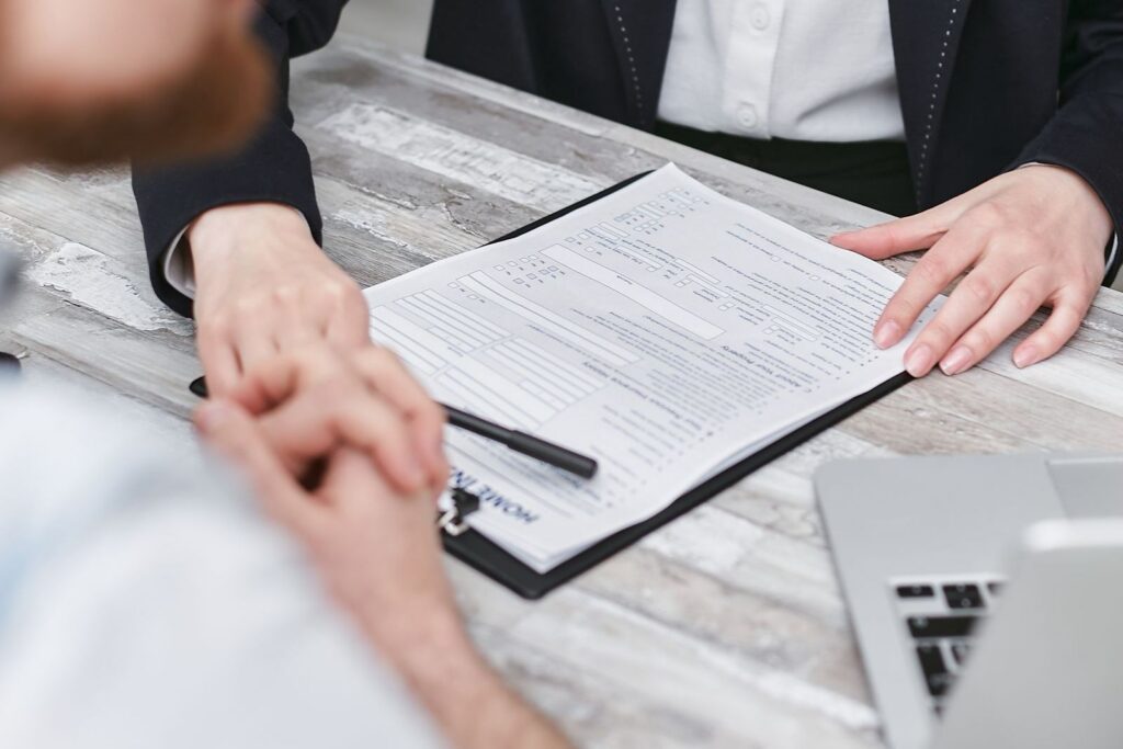 Two people at a table going through a document on a clipboard, with a laptop beside them