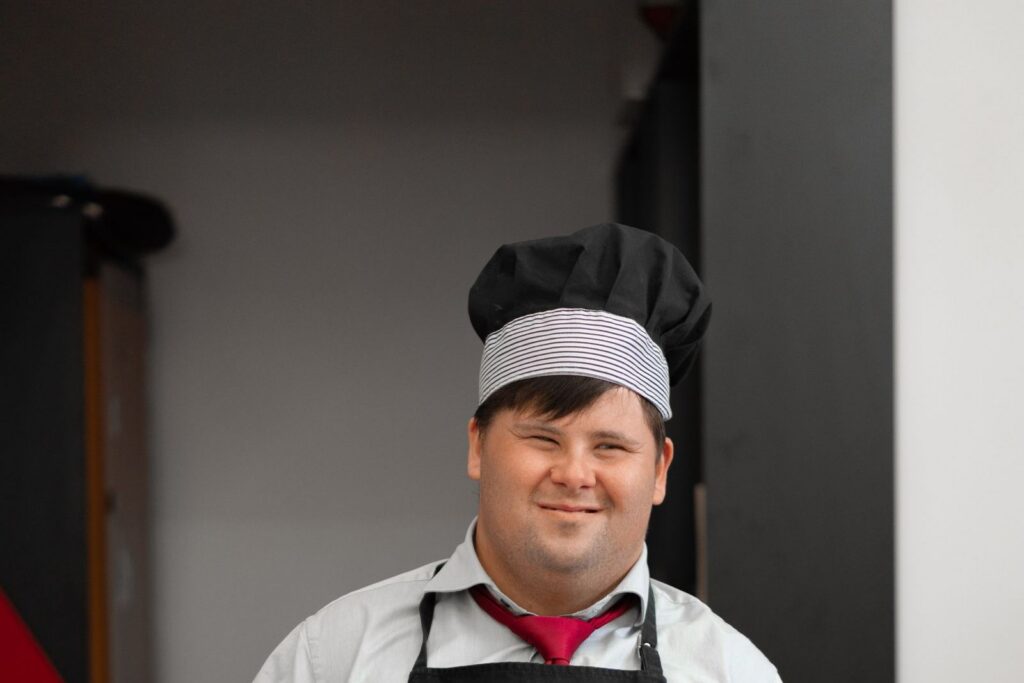 A smiling man in a chef's hat and apron holding a cooking pan