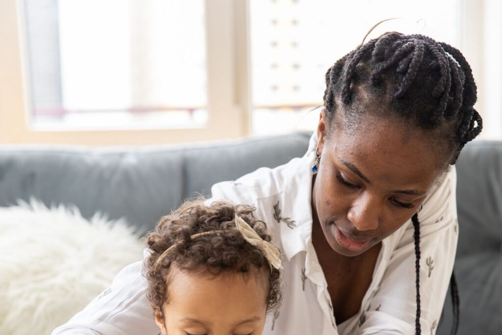 A woman helping a toddler play with wooden blocks at a table at home