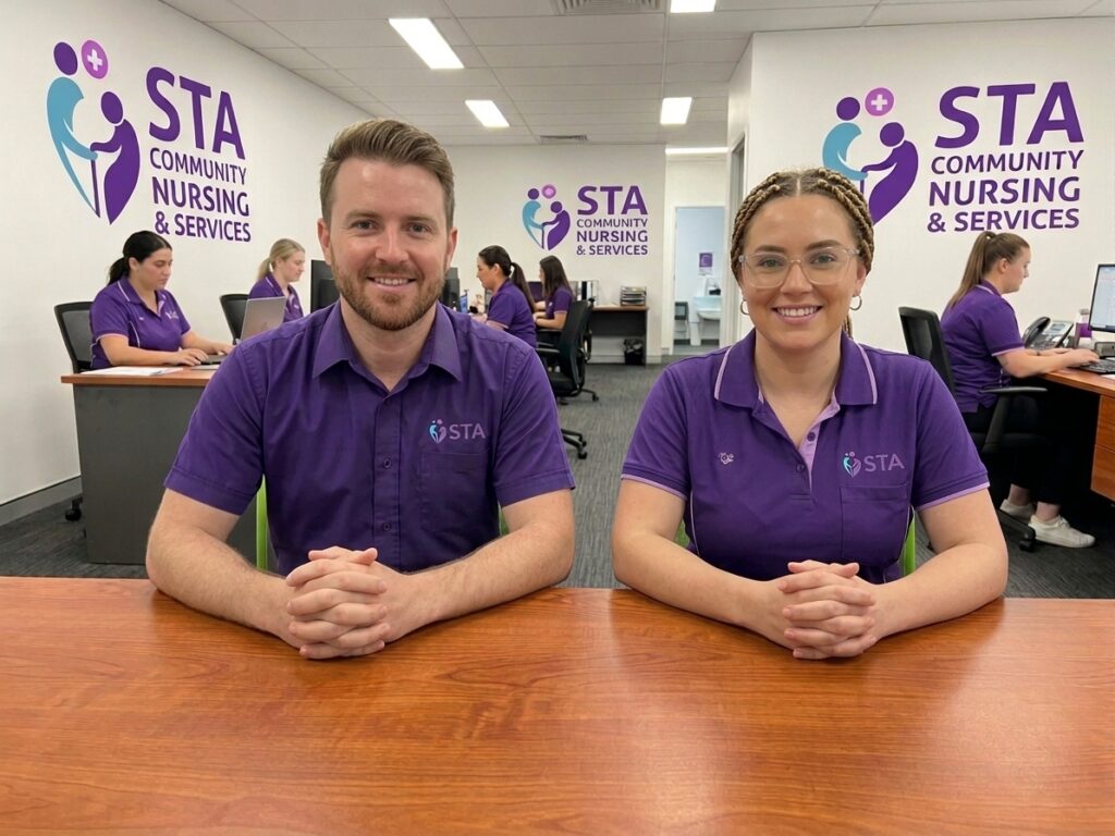 Two STA Community Nursing and Services team members smiling at a desk, with colleagues working behind them