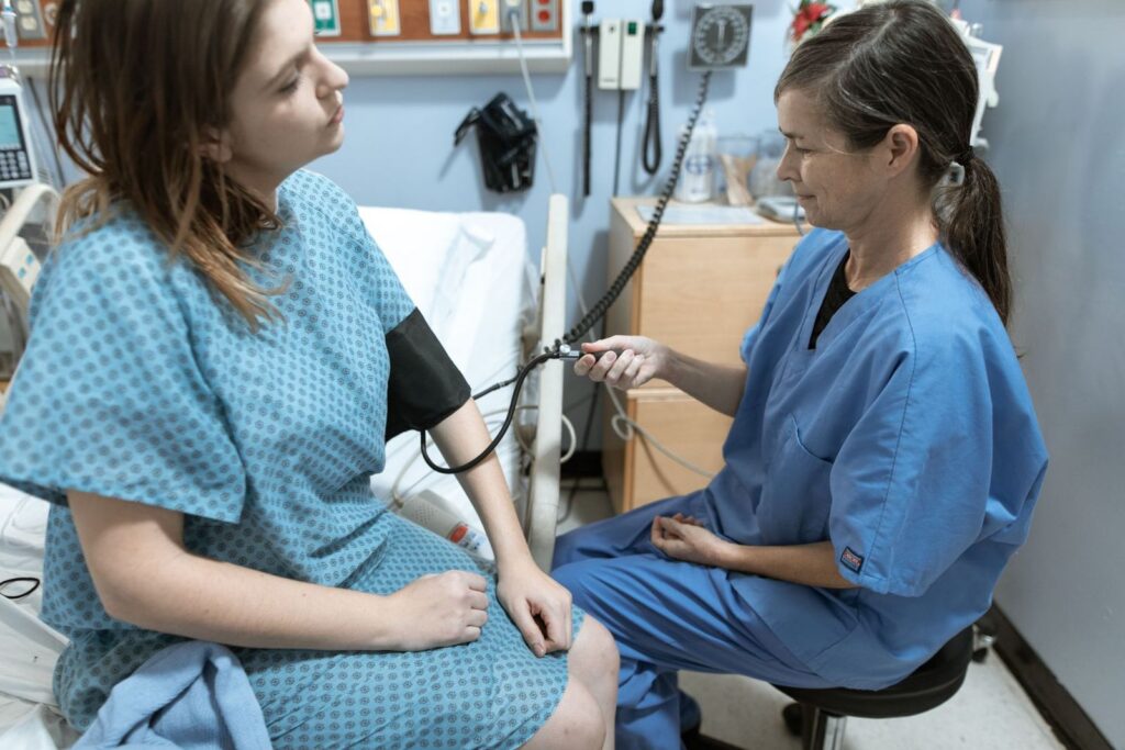 A nurse in blue scrubs taking the blood pressure of a patient in a treatment room