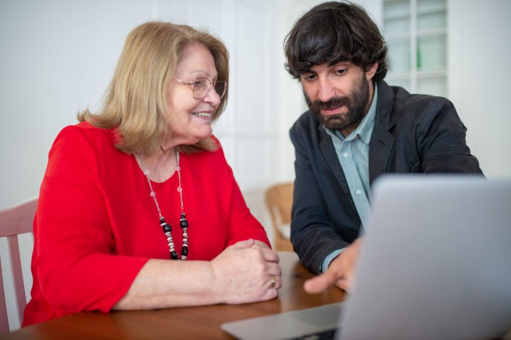 A smiling older woman and a man at a table looking at a laptop together