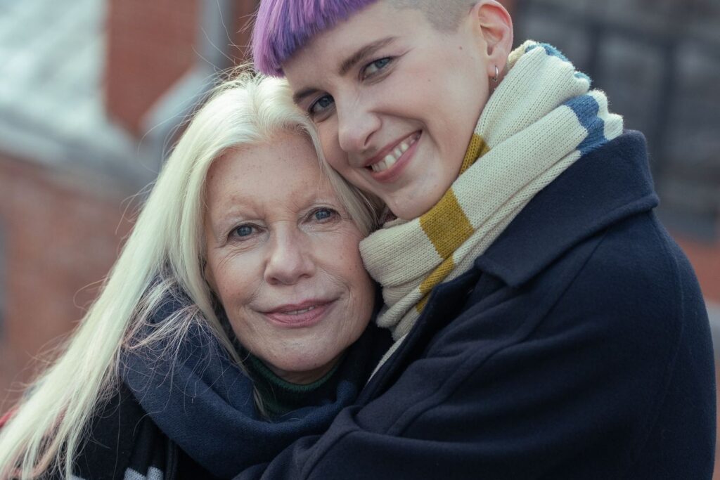 An older woman and a younger woman with a scarf smiling as they hug outdoors