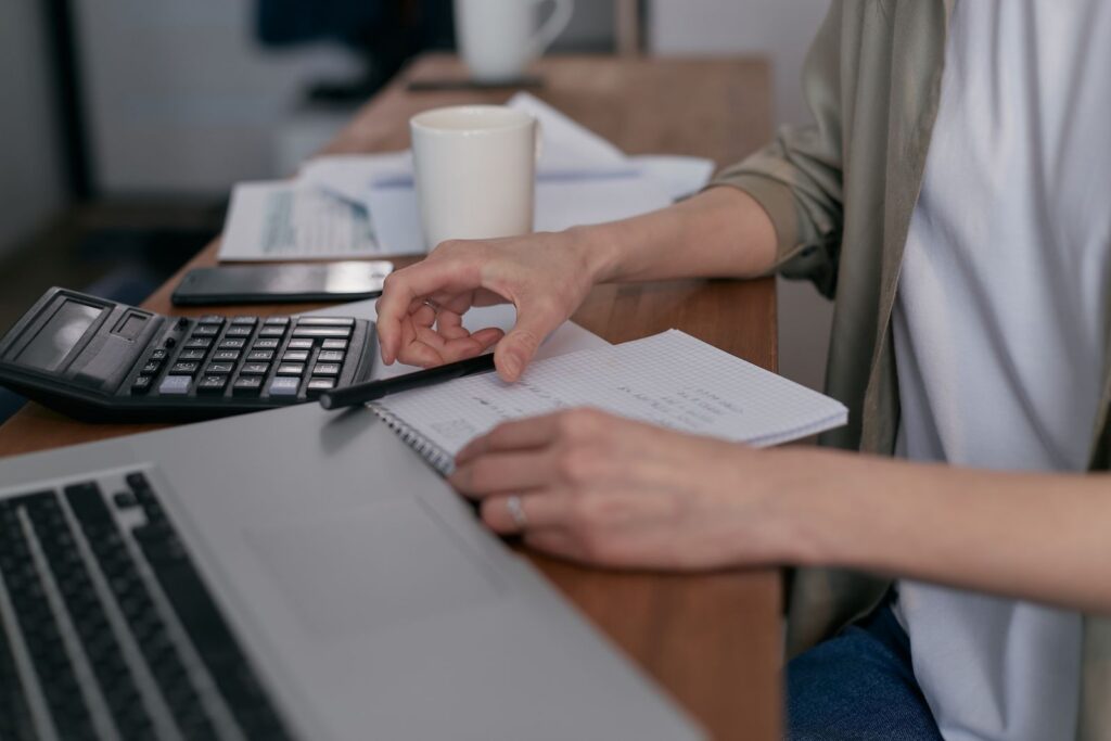 A person working through accounts at a desk with a laptop, calculator and notebook