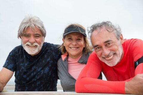 Three older friends leaning on a railing outdoors, smiling together after an outdoor activity