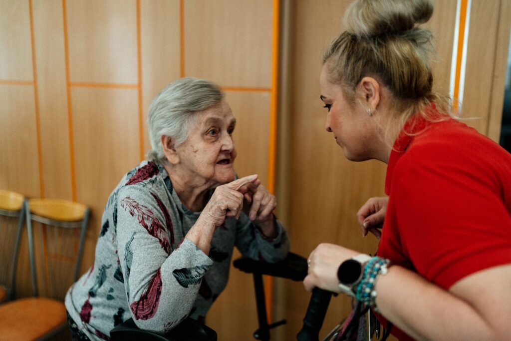A woman in a red top leaning in to talk with an older woman in a bright room
