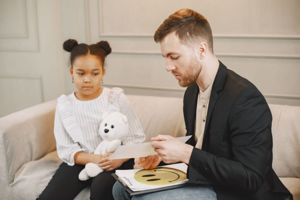 A man showing a picture card to a young girl holding a soft toy during a therapy session