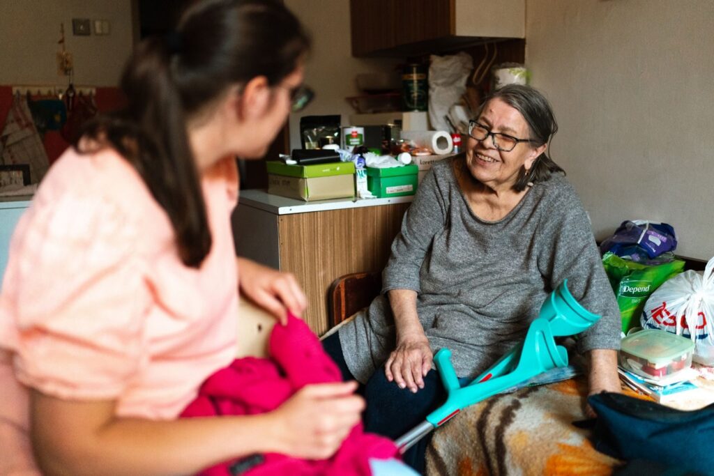 A support worker chatting with an older woman at home, her crutches resting beside her