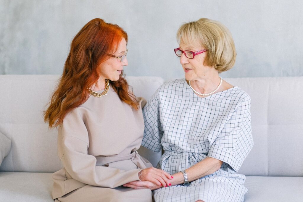 Two women sitting close on a sofa, holding hands and talking